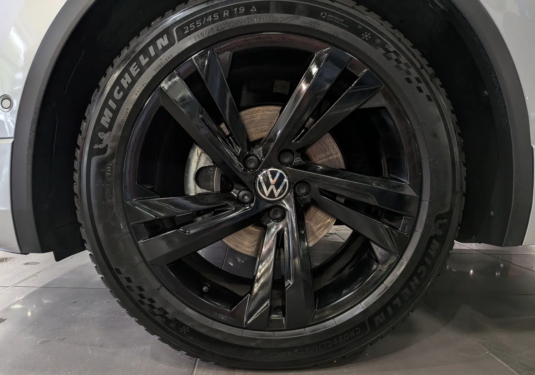 Gros plan sur la jante noire brillante de 19 pouces avec logo Volkswagen, montée sur un pneu Michelin du Tiguan reflet d'argent.