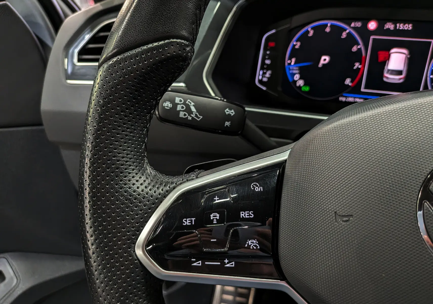 Gros plan sur le volant cuir perforé et les commandes de régulateur du Volkswagen Tiguan 2024, tableau de bord numérique en arrière-plan.