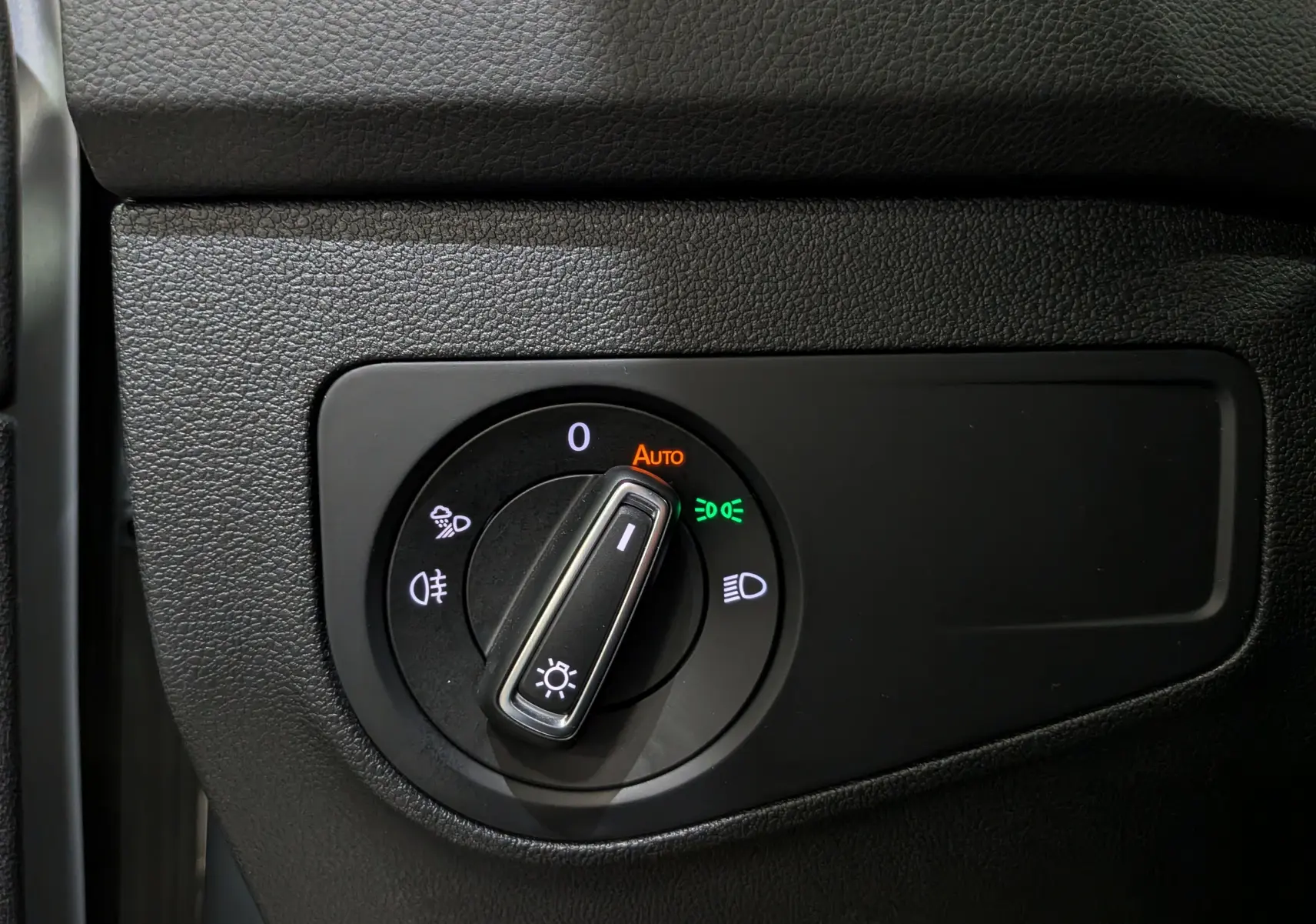 Gros plan sur le sélecteur de phares du Volkswagen Tiguan 2024, avec éclairage automatique activé, intérieur noir texturé.