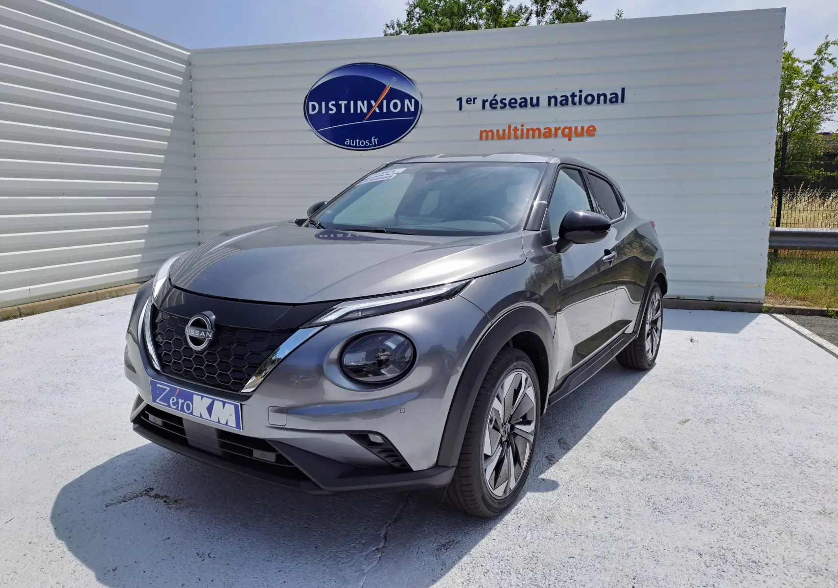 Nissan Juke Hybrid gris squale vu de 3/4 avant droit, avec calandre noire et jantes alliage modernes.