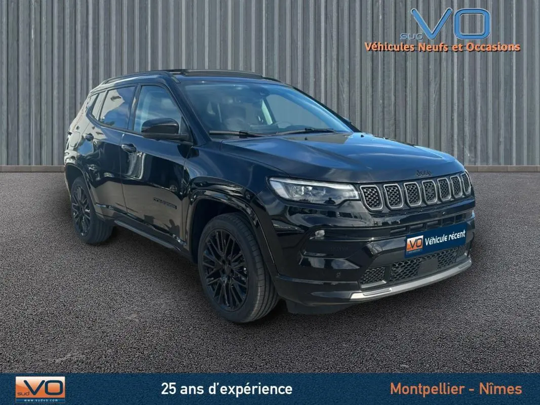 Jeep Compass noir en 3/4 avant droit, avec barres de toit et jantes alliage noires, stationné devant un mur métallique.