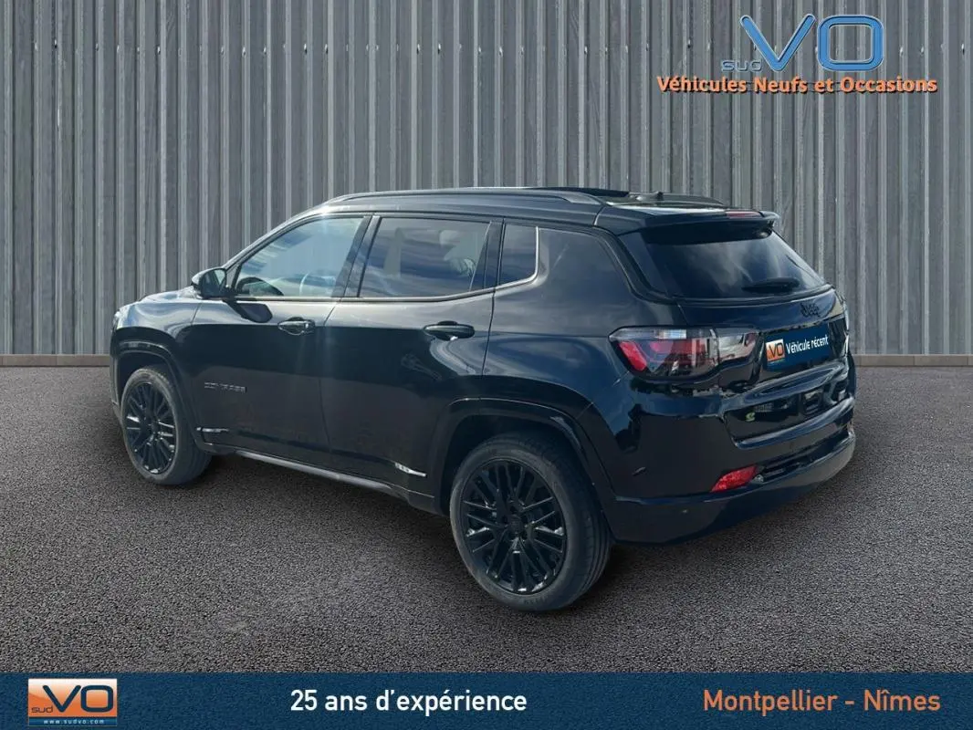 Vue 3/4 arrière droite d'un Jeep Compass noir 2023 avec jantes alliage noires et barres de toit visibles.