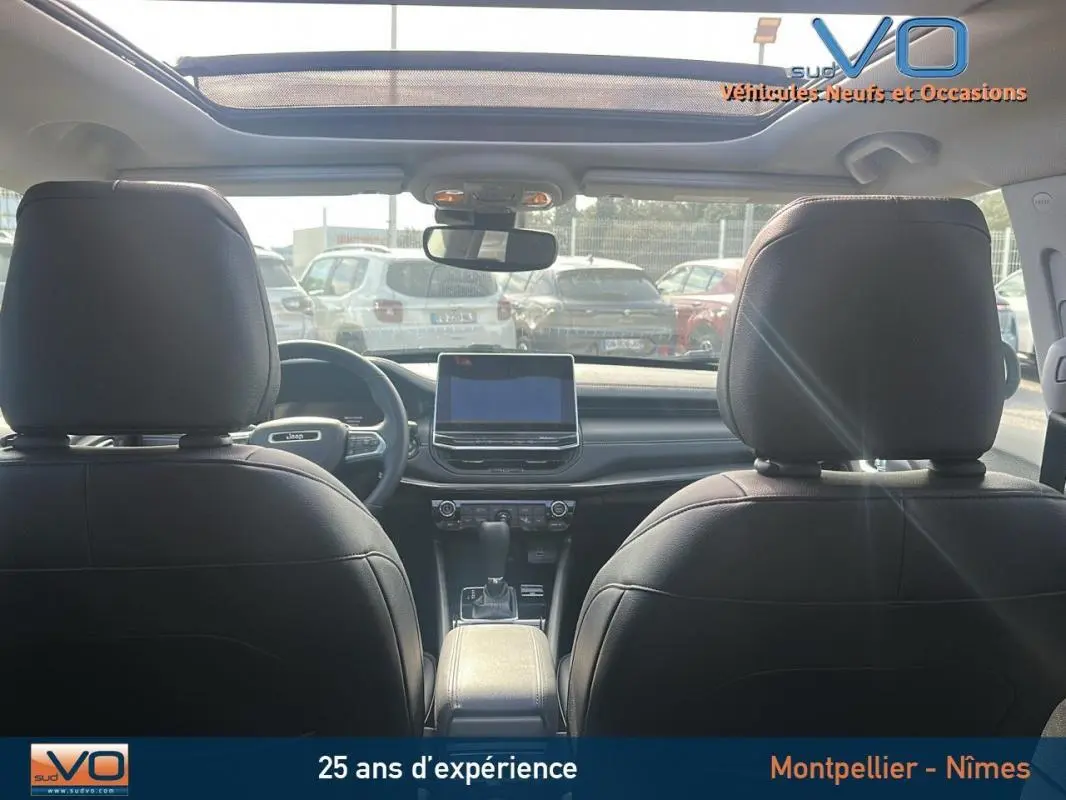 Vue intérieure arrière du Jeep Compass noir 2023 avec toit ouvrant panoramique et écran tactile central.