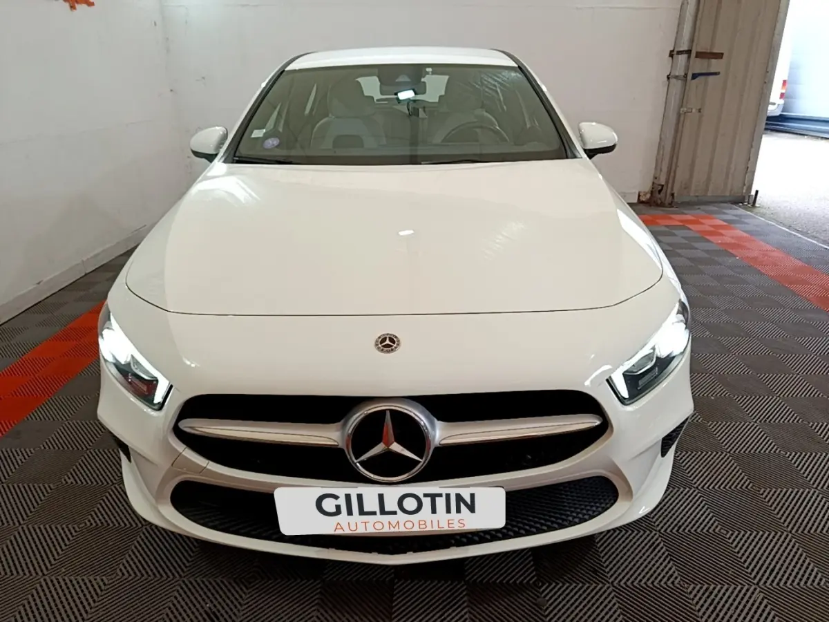 Vue avant d'une Mercedes Classe A Berline blanche avec phares LED allumés dans un garage.