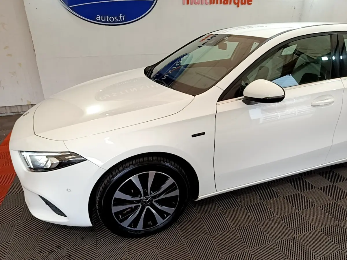 Vue 3/4 avant droit d'une Mercedes Classe A Berline A 250 e Business Line blanche avec jantes noires distinctives.