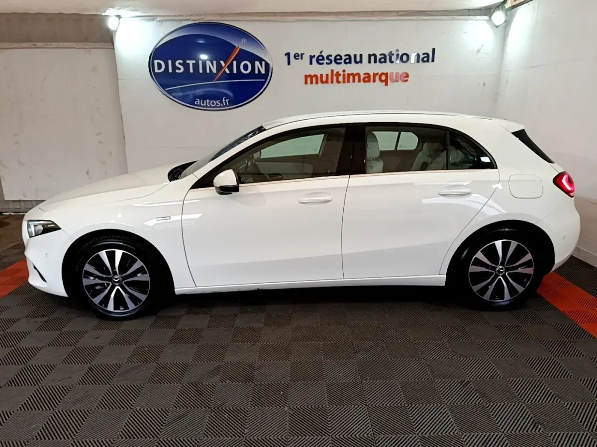 Profil côté gauche d'une Mercedes Classe A Berline blanche, vue en intérieur avec jantes alliage et feux arrière allumés.