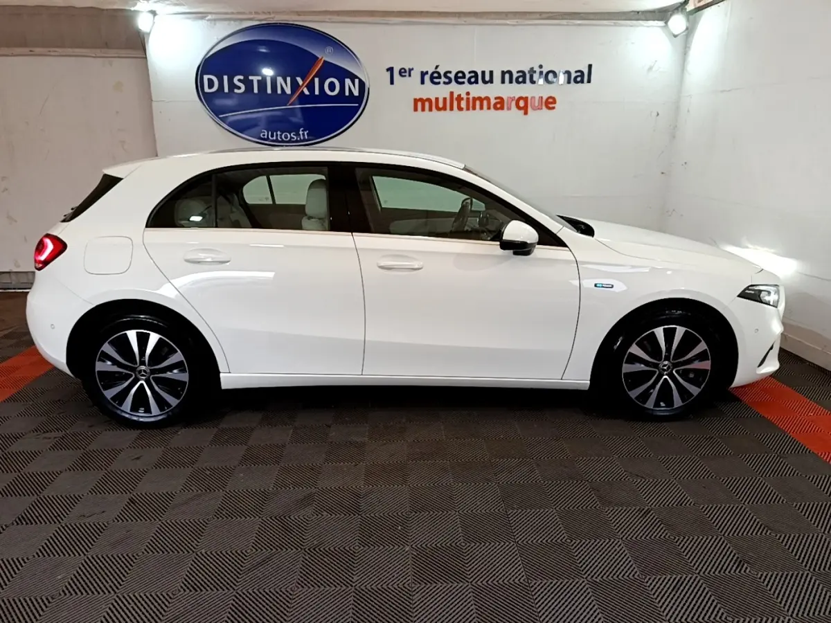 Vue latérale droite d'une Mercedes Classe A Berline blanche, hybride rechargeable, avec jantes alliage et feux arrière allumés.