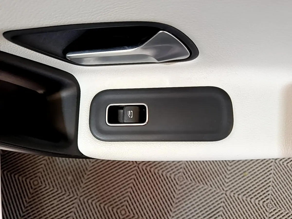 Gros plan sur la commande de lève-vitre électrique sur la porte intérieure blanche d'une Mercedes Classe A Berline.