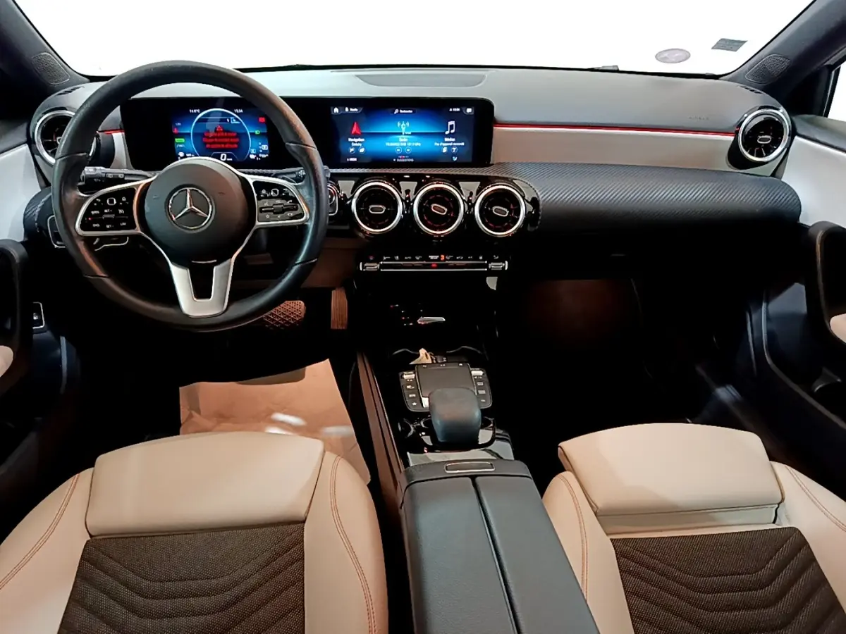 Vue intérieure avant de la Mercedes Classe A 250 e Business Line 2020, volant cuir noir et sièges beige avec console centrale noire.