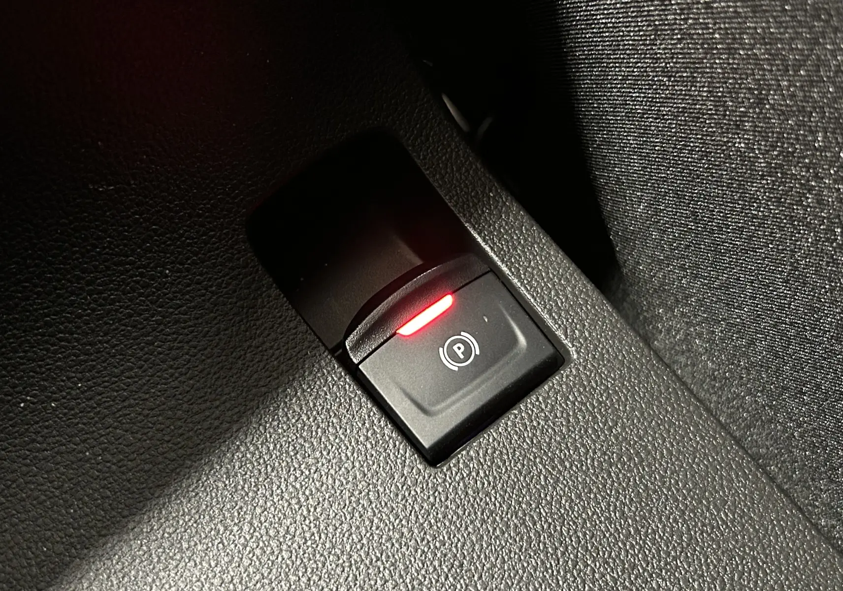 Détail du bouton de frein à main électrique allumé sur la console intérieure d'un Dacia Jogger gris schiste métal.