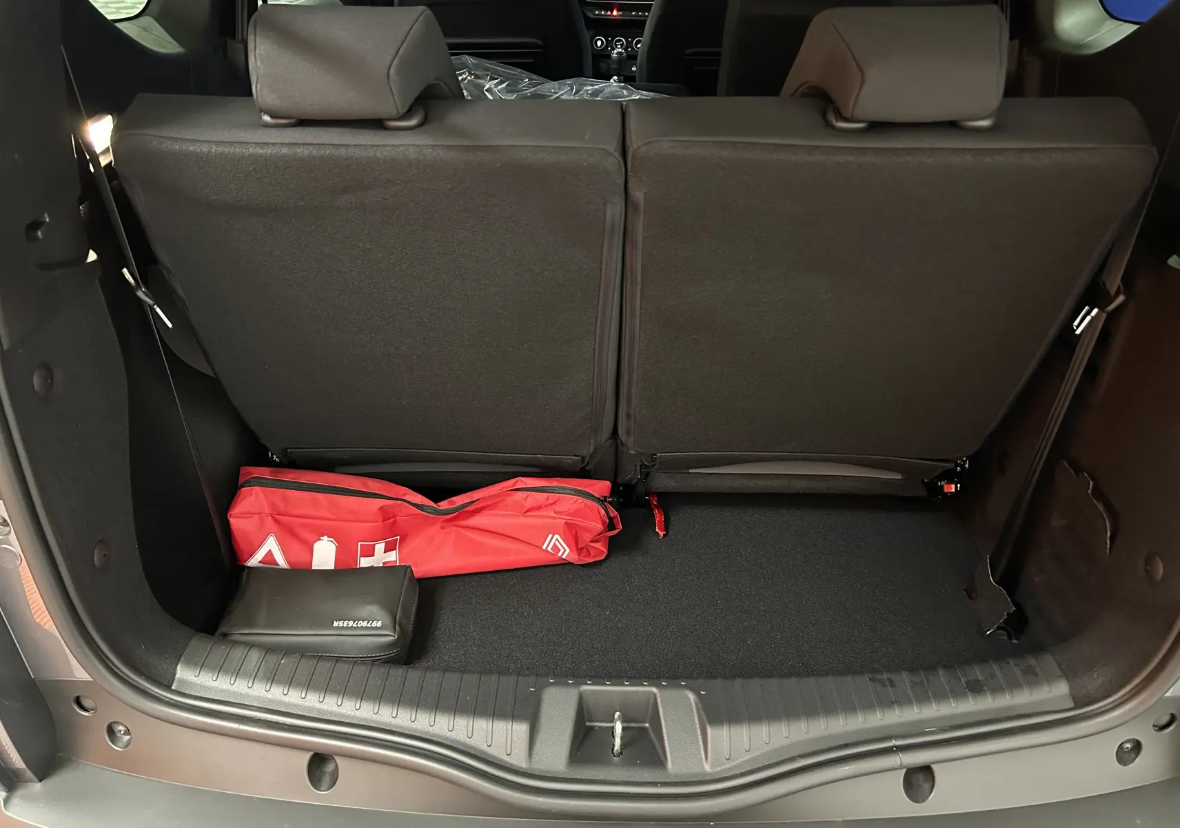Coffre ouvert d’un Dacia Jogger gris schiste, vue arrière montrant la banquette arrière et un kit de sécurité rouge.