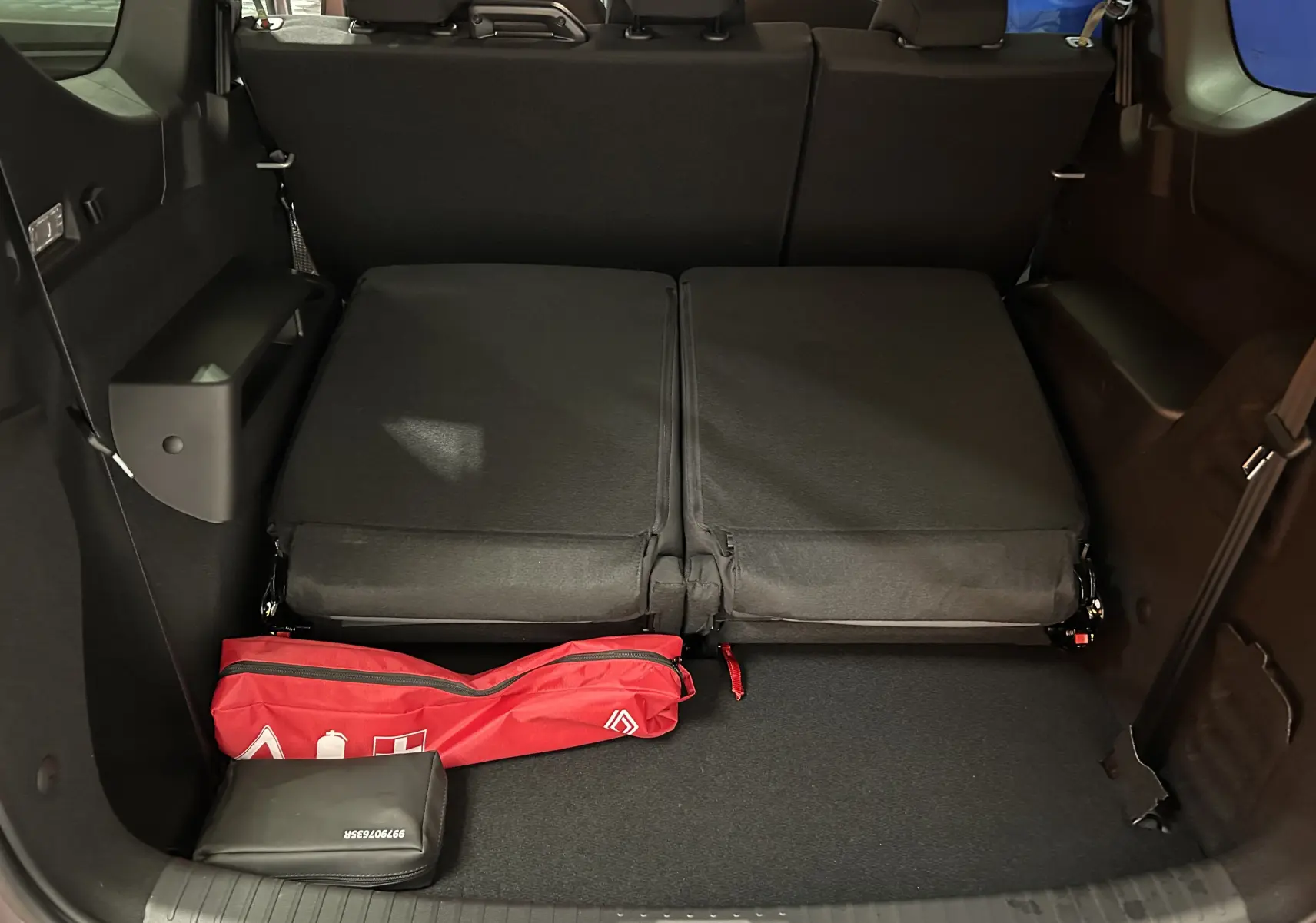 Vue intérieure du coffre du Dacia Jogger gris schiste avec sièges arrière rabattus et trousse de secours rouge visible.
