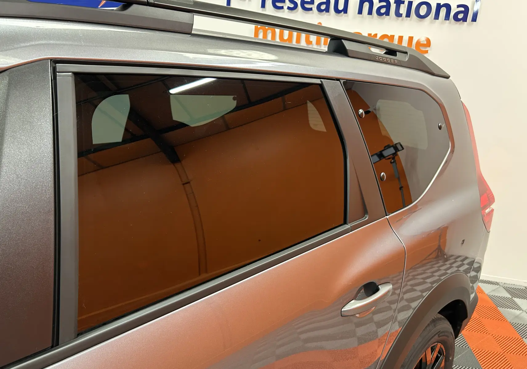 Vue latérale droite du Dacia Jogger gris schiste métal, mettant en valeur les vitres teintées et le toit avec barres de toit.