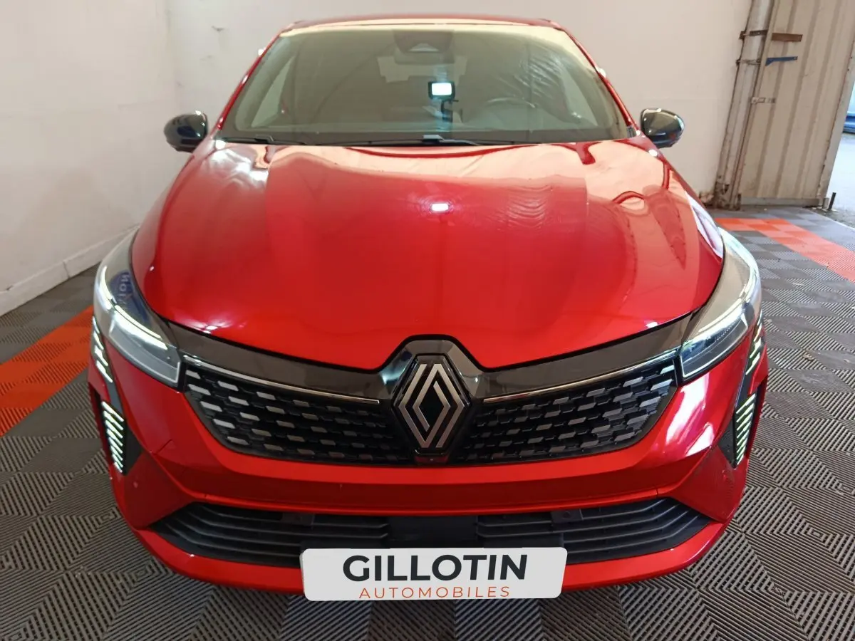 Vue avant d'une Renault Clio Techno TCe 90 rouge 2024 avec calandre noire et feux LED allumés en intérieur.