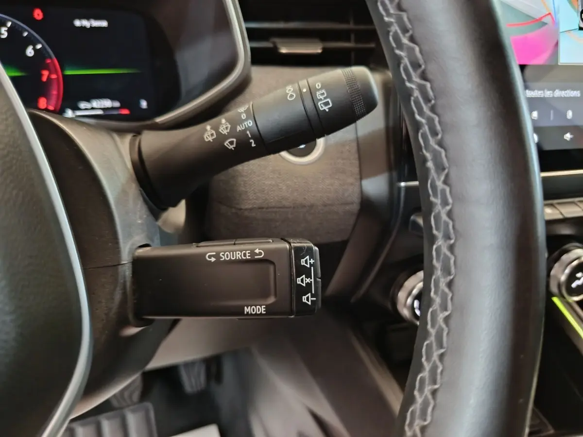 Gros plan sur la manette multifonctions à gauche du volant de la Renault Clio rouge 2024, avec tableau de bord partiellement visible.