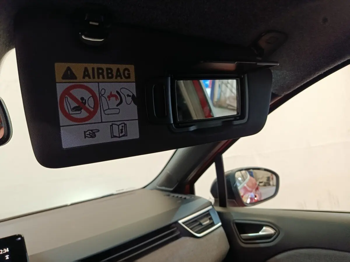 Vue intérieure côté conducteur de la Renault Clio rouge 2024, miroir de pare-soleil ouvert avec avertissement airbag visible.