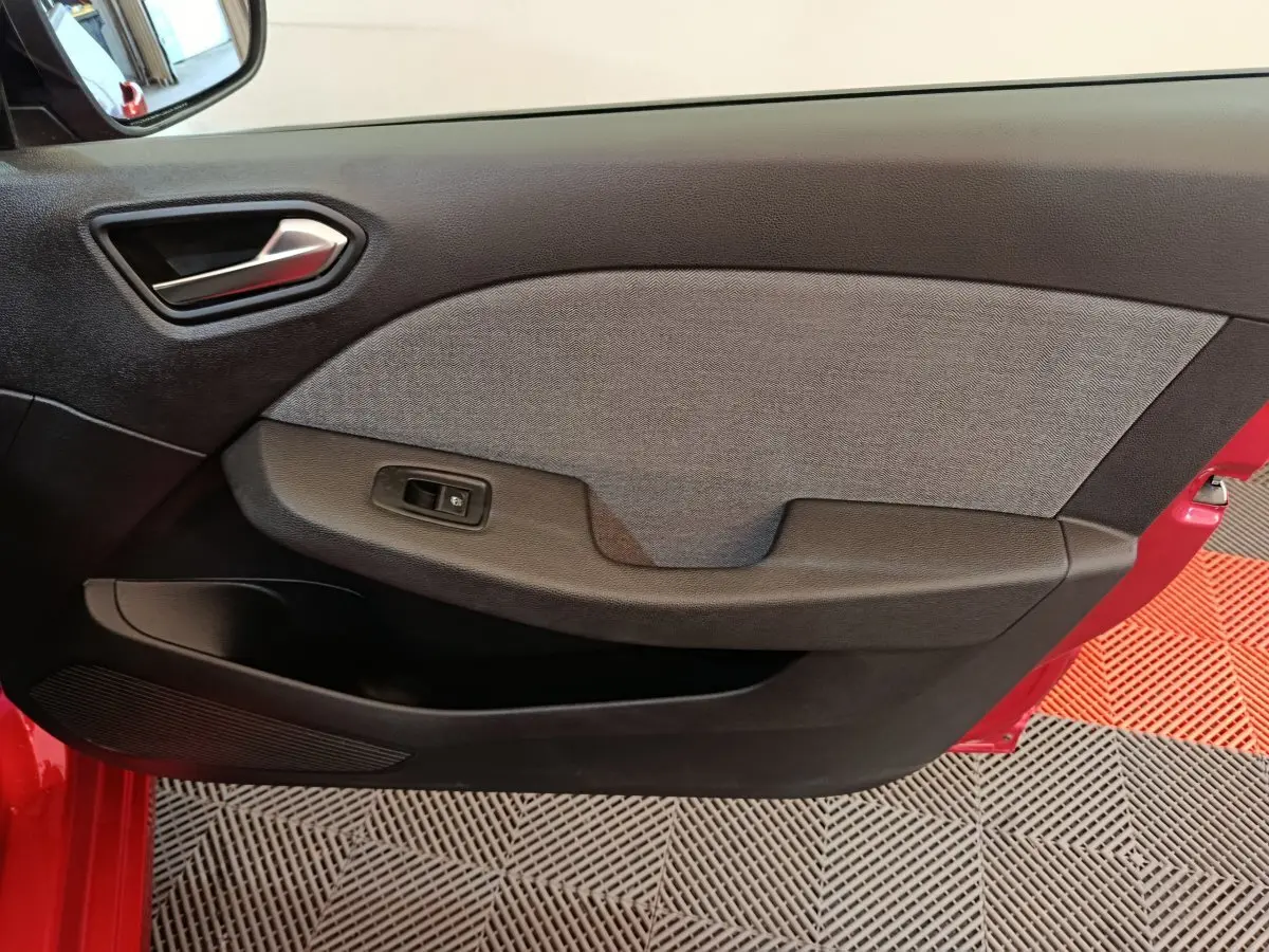 Vue intérieure du panneau de porte avant gauche de la Renault Clio rouge 2024, avec poignée argentée et bouton de commande de vitre.