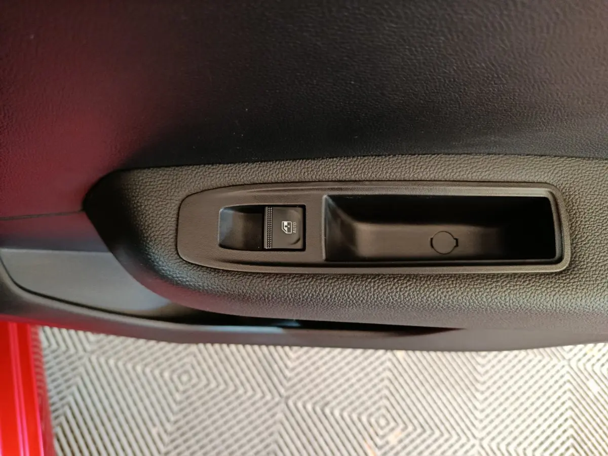 Gros plan sur le bouton de commande de la vitre électrique côté conducteur d'une Renault Clio rouge 2024.