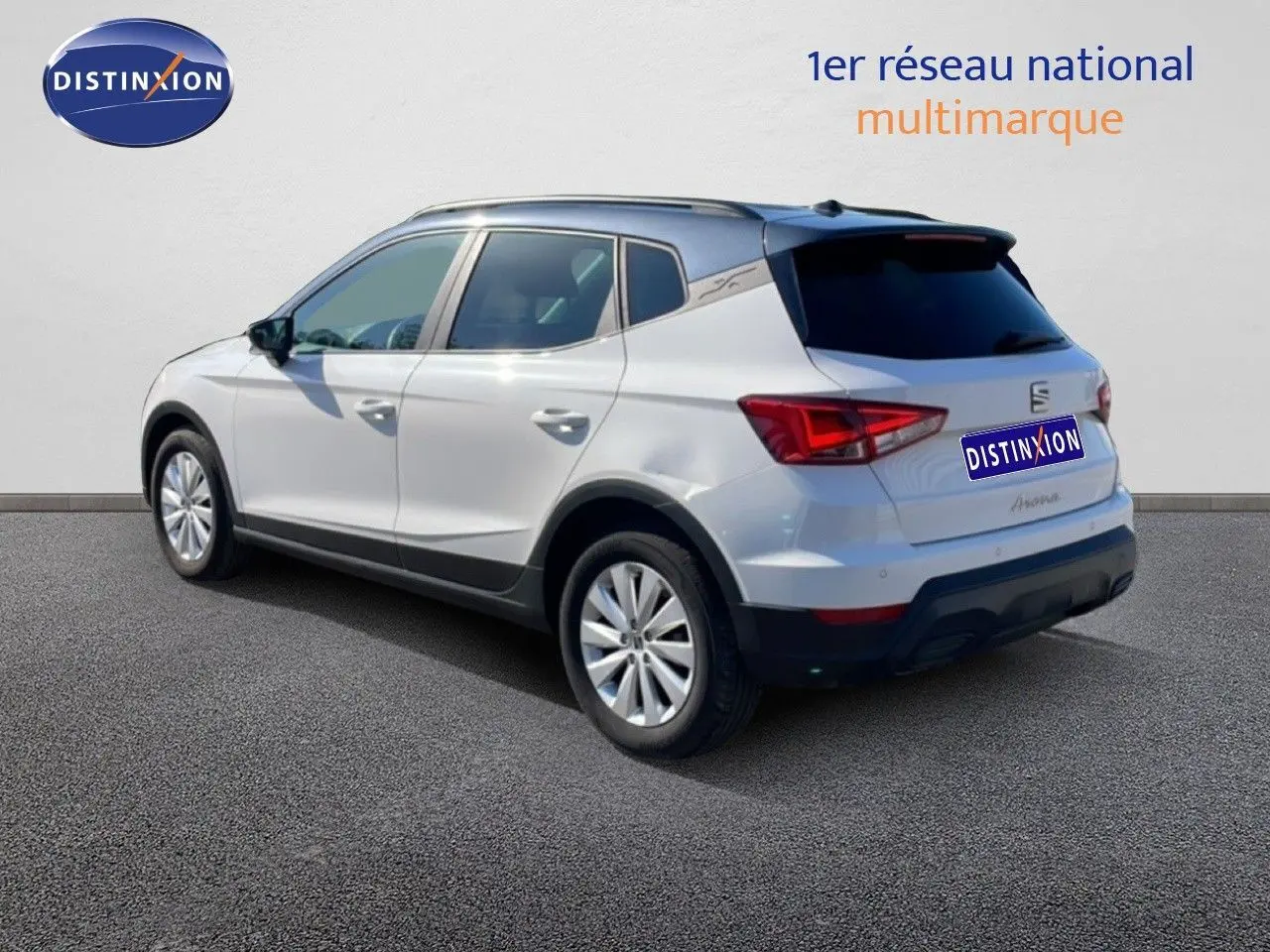 SEAT Arona blanc avec toit gris, vue 3/4 arrière côté gauche, sur sol bitumé devant un mur clair.