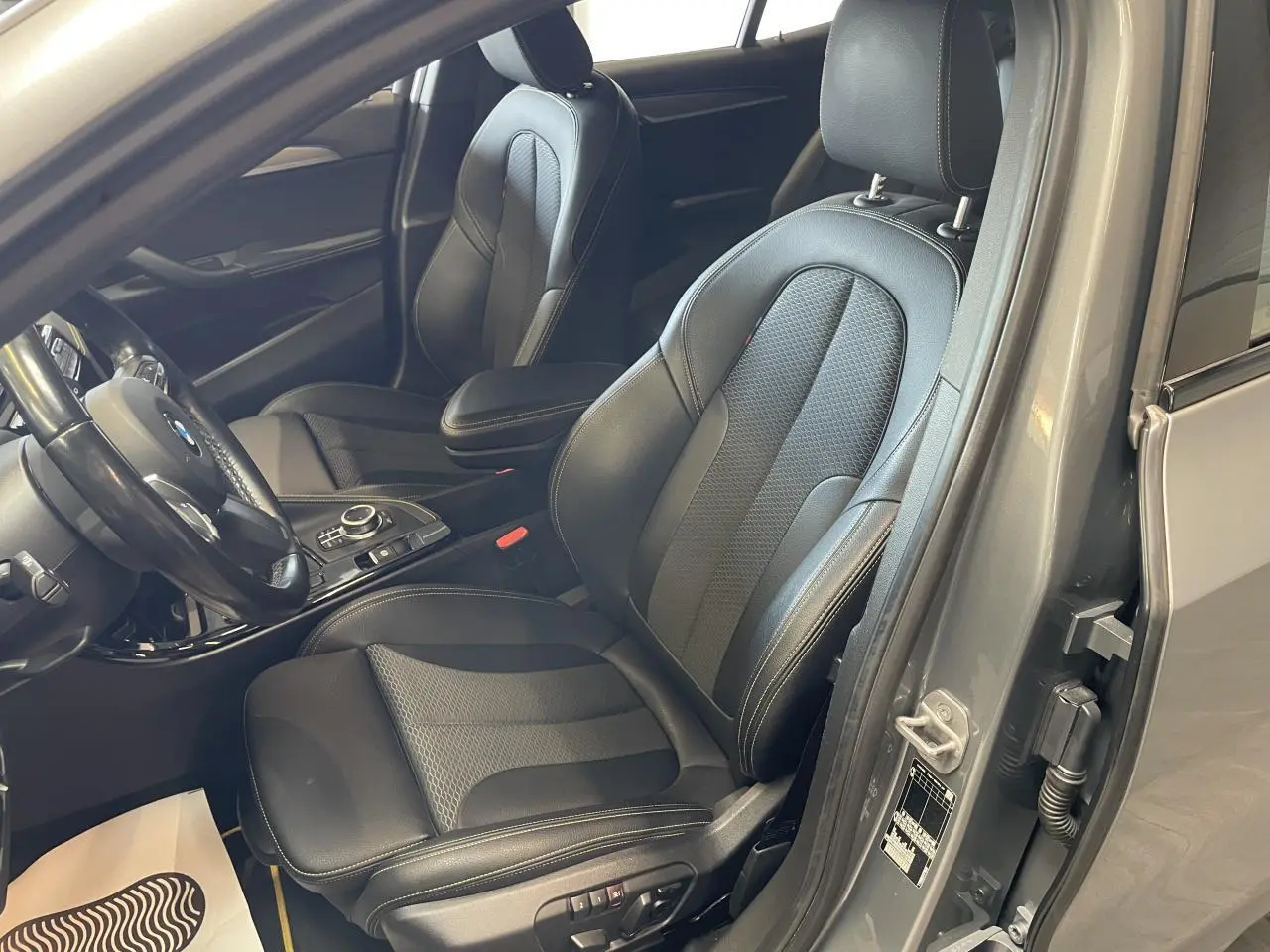 Vue intérieure côté conducteur d'une BMW X2 M Sport X 2022 gris foncé avec sièges en similicuir noir et surpiqûres contrastantes.