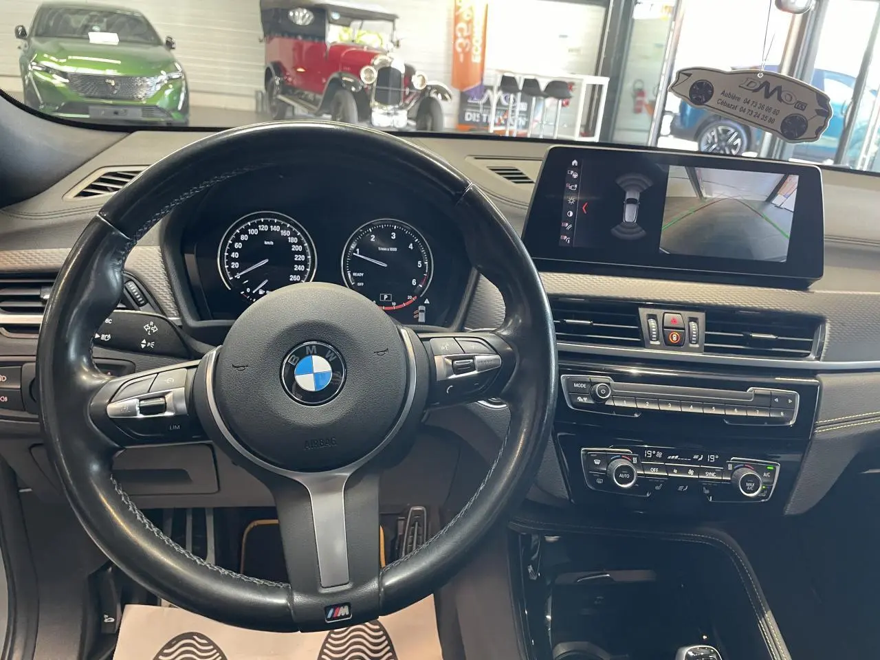 Vue intérieure centrée sur le volant cuir M et le tableau de bord avec écran multimédia du BMW X2 gris foncé.