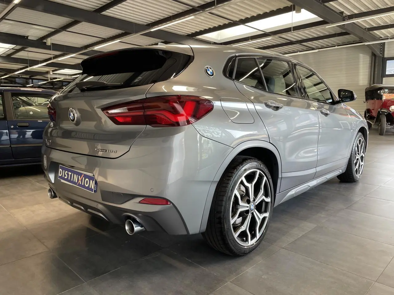 BMW X2 sDrive 18d gris foncé vue 3/4 arrière droit avec jantes 19 pouces style 722 M et double sortie d’échappement chromée.