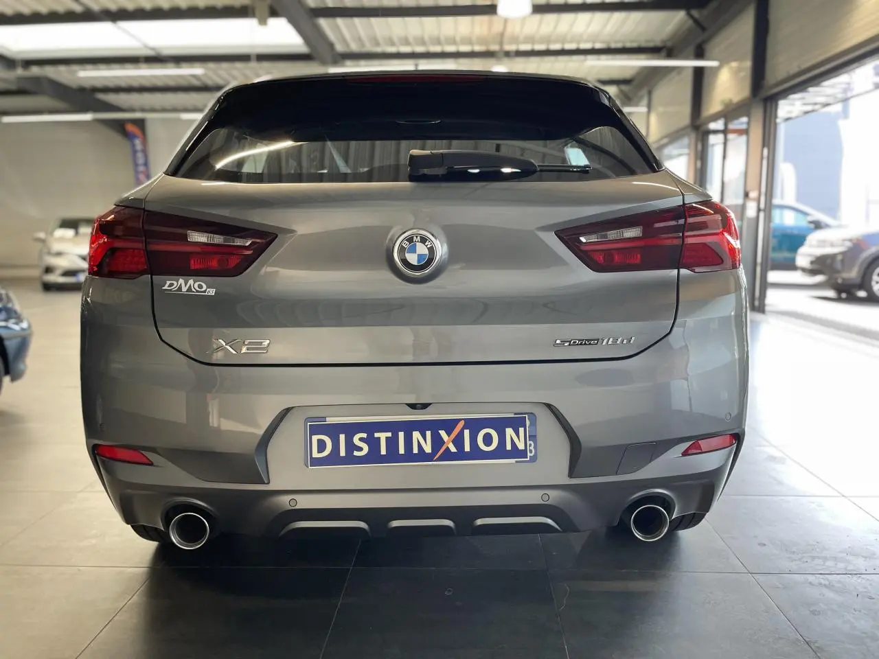 Vue arrière d'une BMW X2 sDrive18d gris foncé avec double sortie d'échappement chromée en intérieur showroom.