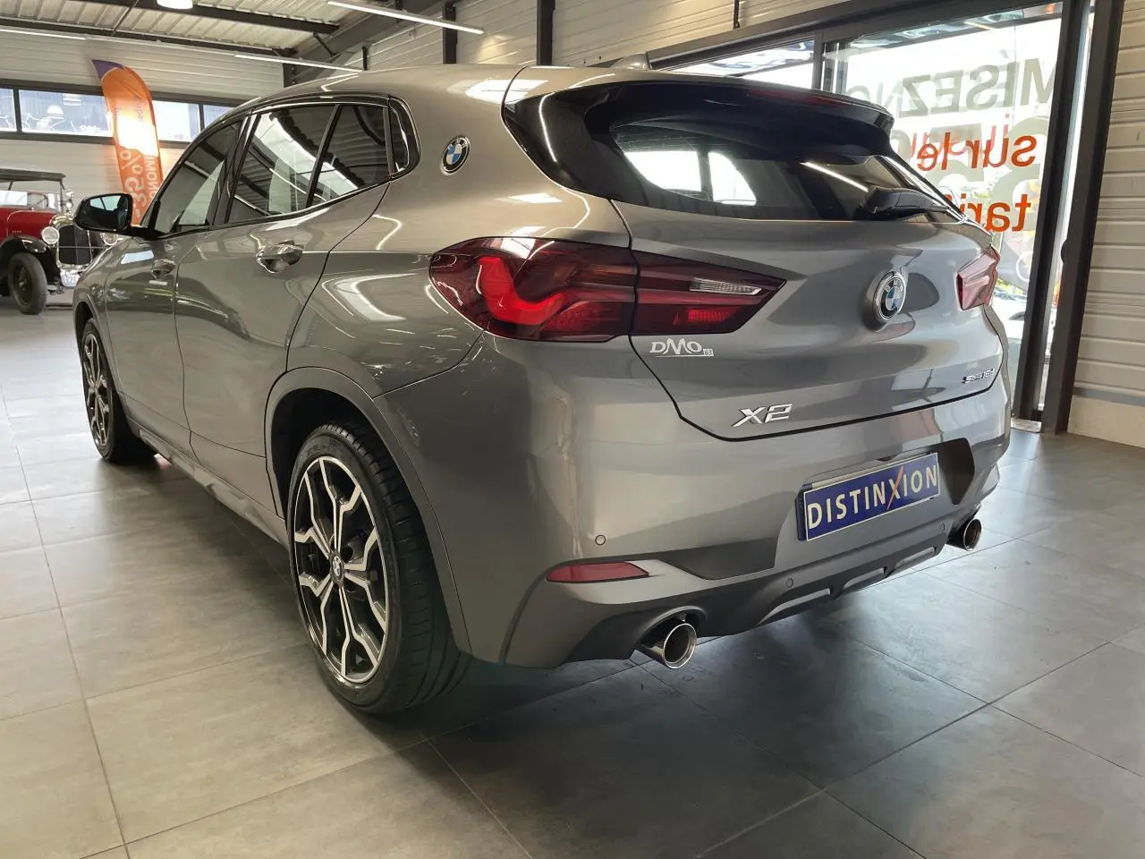 BMW X2 sDrive 18d gris foncé vue 3/4 arrière droit, avec jantes alliage 19" style 722 M et double sortie d’échappement chromée.