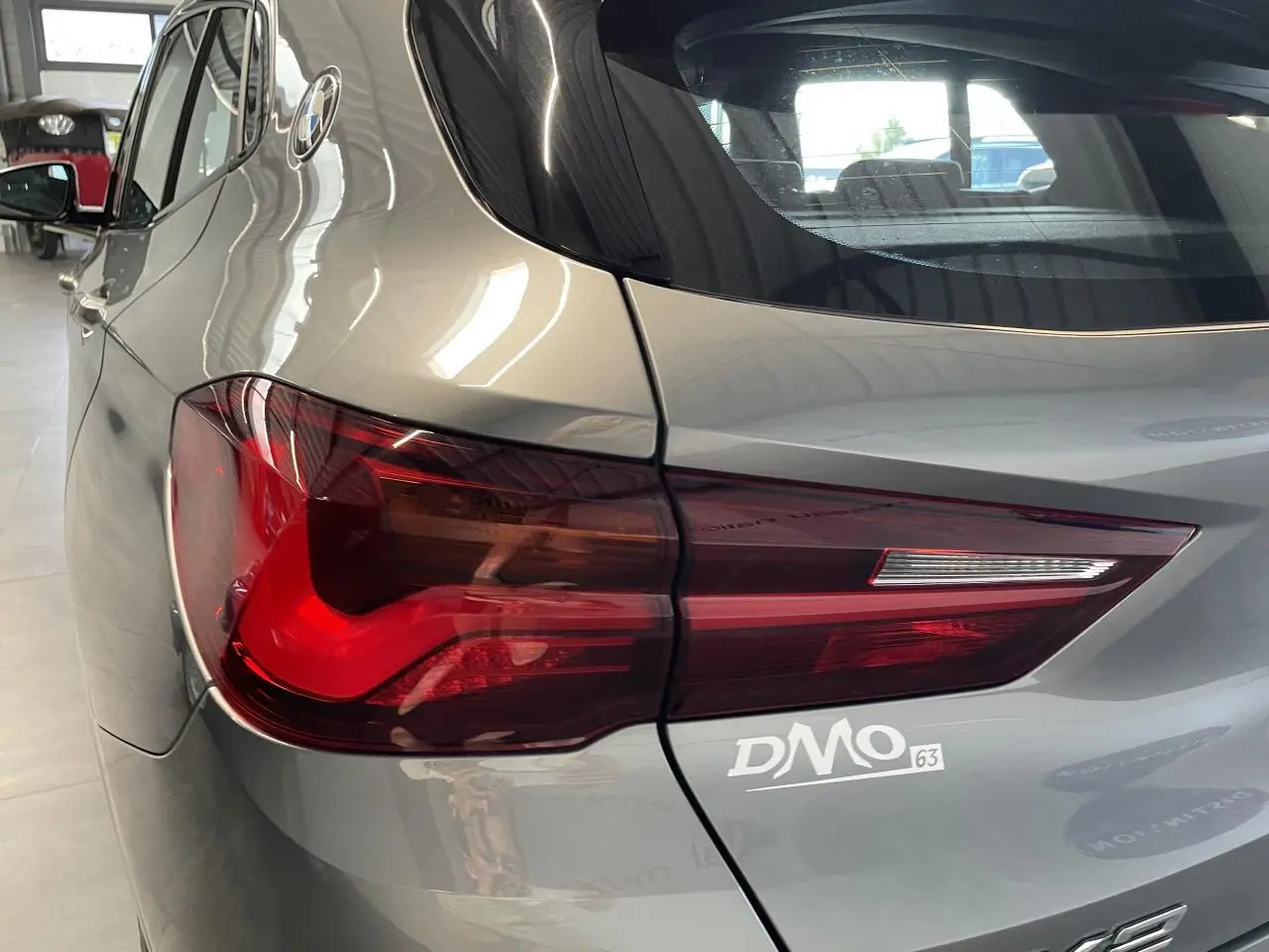 Gros plan sur le feu arrière gauche d’une BMW X2 gris foncé, mettant en valeur la finition M Sport X et le logo DMO.