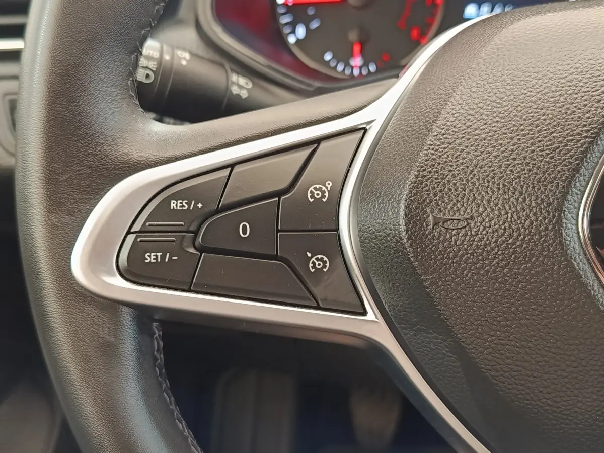Gros plan sur la partie gauche du volant cuir noir de la Renault Clio blanc, avec commandes de régulateur de vitesse.