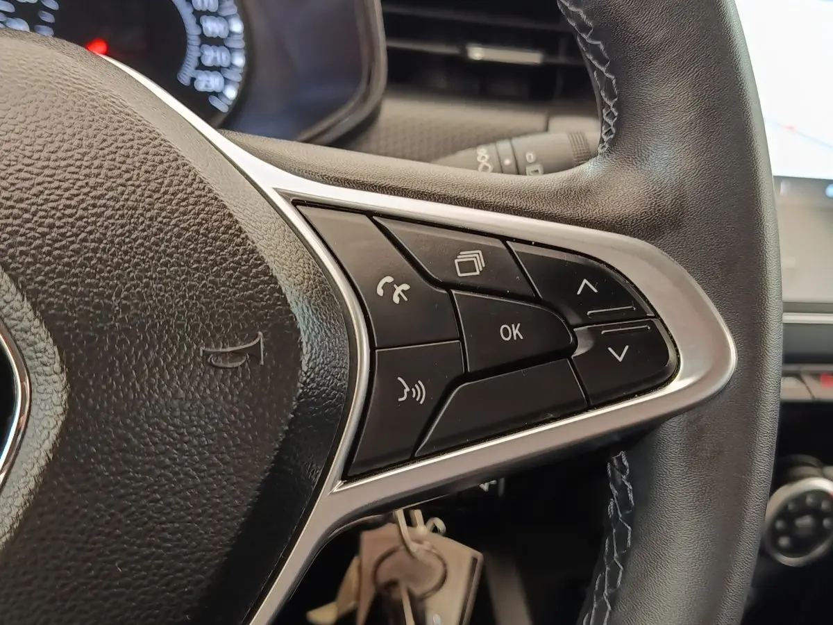 Gros plan sur les commandes multifonctions noires du volant en cuir noir de la Renault Clio Business blanche.