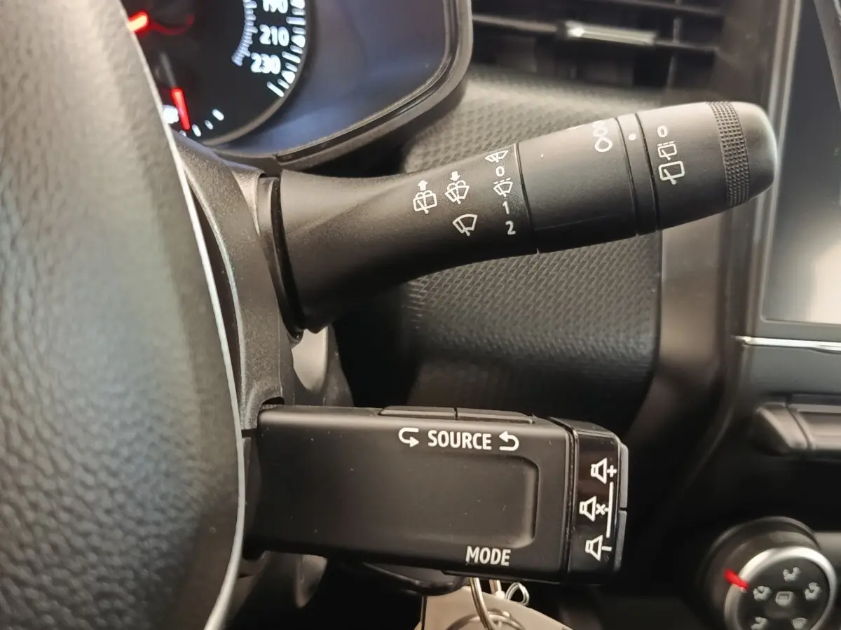 Gros plan sur la commande multifonction gauche du tableau de bord d’une Renault Clio blanche, intérieur noir.