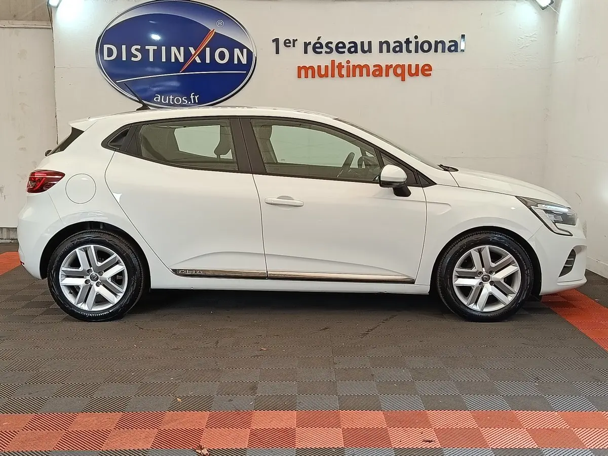 Profil droit d'une Renault Clio Business TCe 100 GPL blanche 2021 avec jantes alliage et logo Distinxion en arrière-plan.