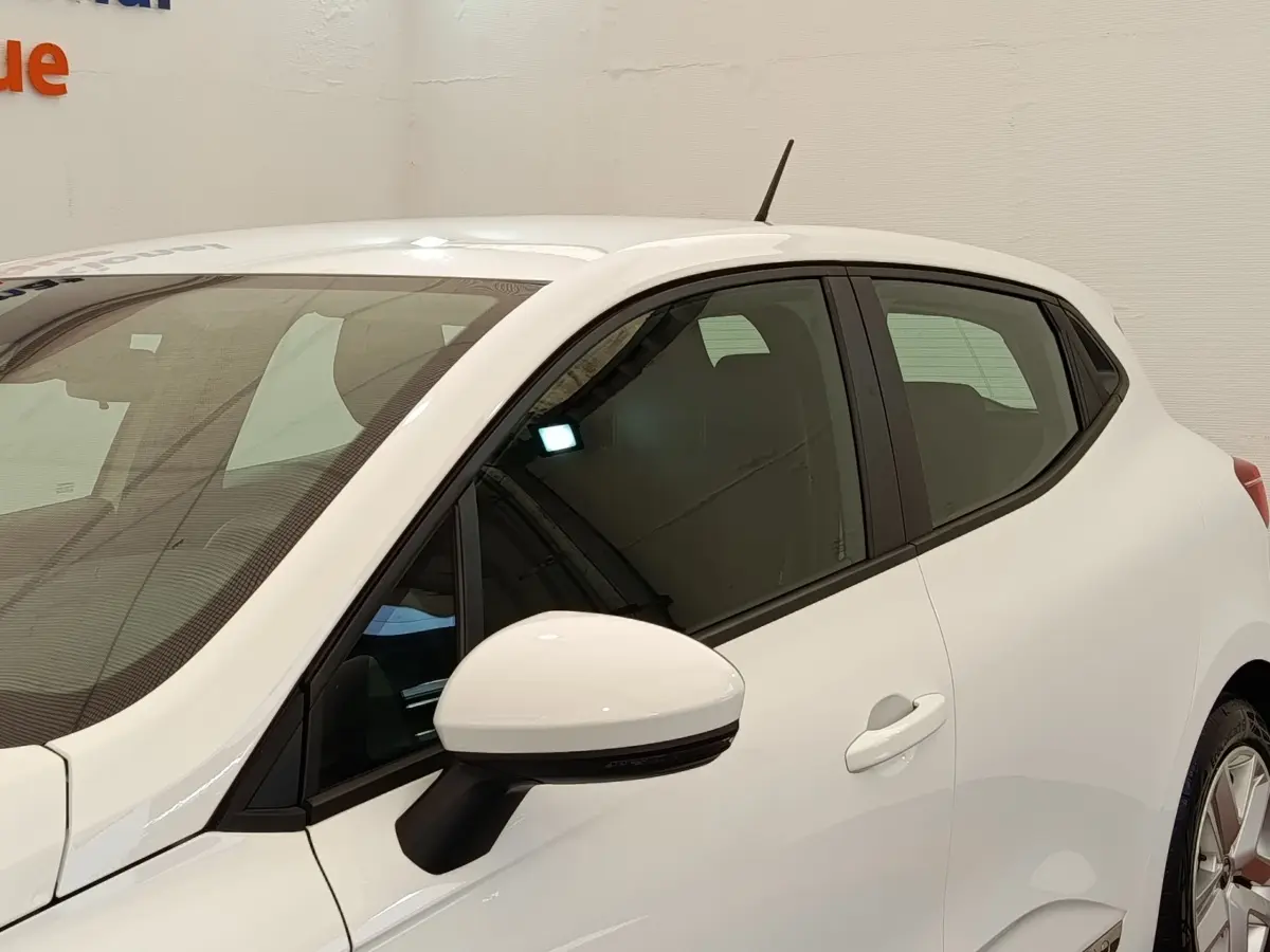 Vue côté gauche avant d'une Renault Clio Business blanche, avec rétroviseur blanc et vitres teintées.