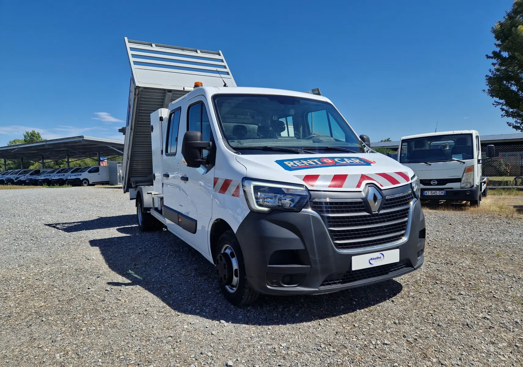 Renault Master blanc vue 3/4 avant droit avec benne relevée et marquages rouges sur capot et portières.