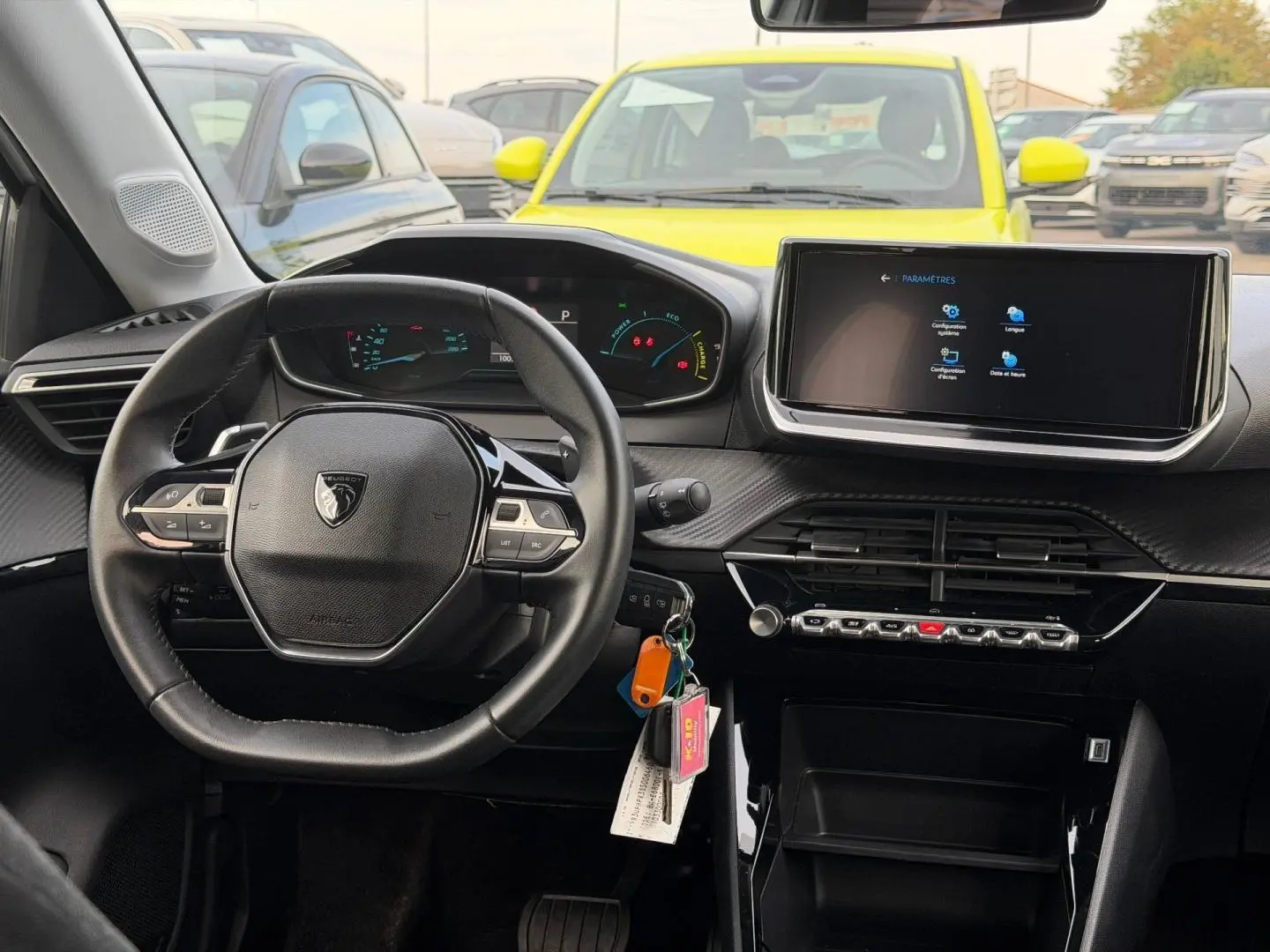 Vue intérieure centrée sur le volant Peugeot 208 blanc Okénite, avec écran tactile et tableau de bord numérique.