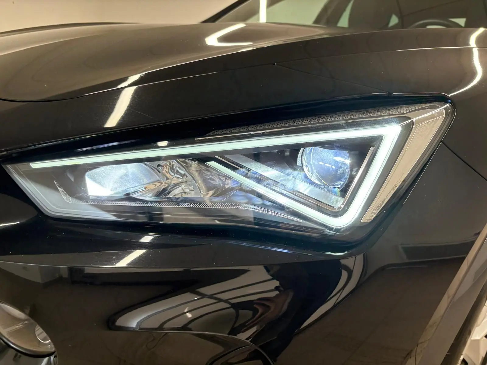 Gros plan sur le phare avant droit allumé du CUPRA Formentor 1.5 TSI noir minuit, soulignant son design anguleux LED.