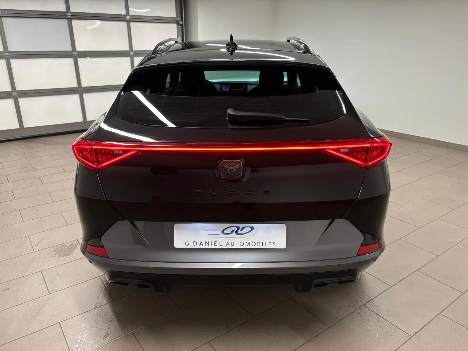 Vue arrière d'un CUPRA Formentor noir minuit 2024 avec feux arrière LED continus et hayon électrique en intérieur showroom.