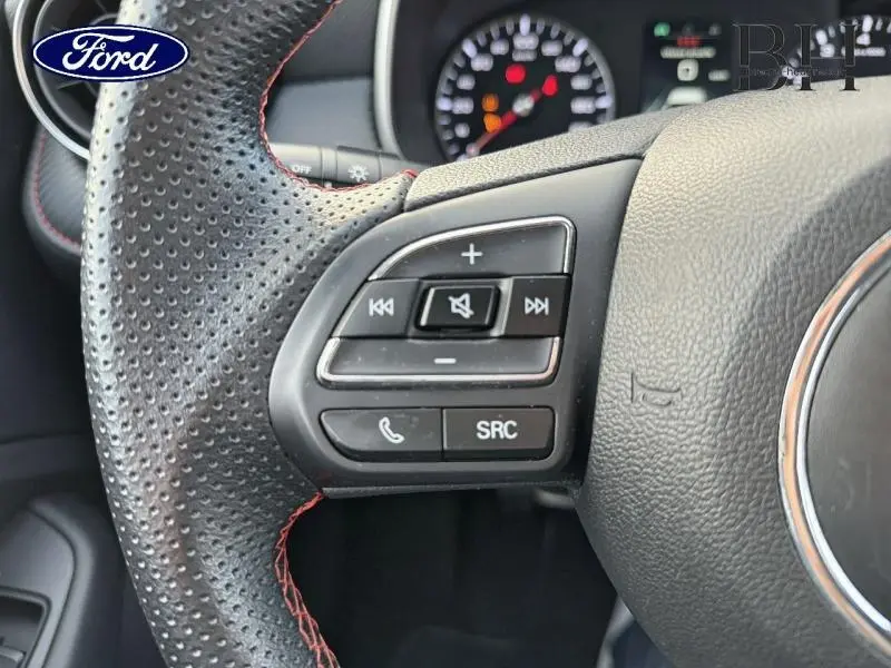 Gros plan sur les commandes audio et téléphone au volant perforé noir avec surpiqûres rouges d'une MG ZS Cosmic Silver.