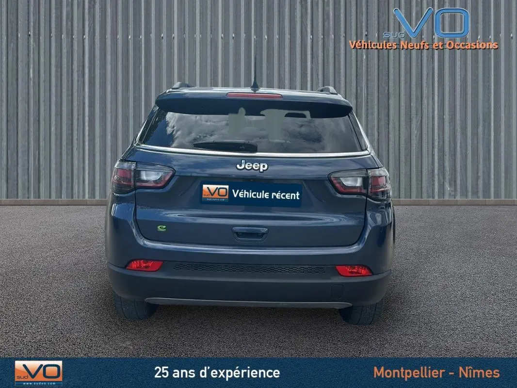 Vue arrière d'un Jeep Compass bleu 2023 avec barres de toit et feux arrière LED visibles sur sol goudronné.