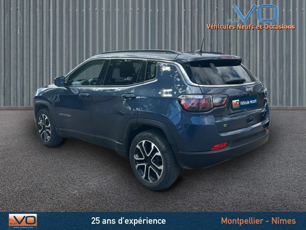 Jeep Compass bleu 3/4 arrière côté gauche, avec barres de toit et jantes 18 pouces visibles.
