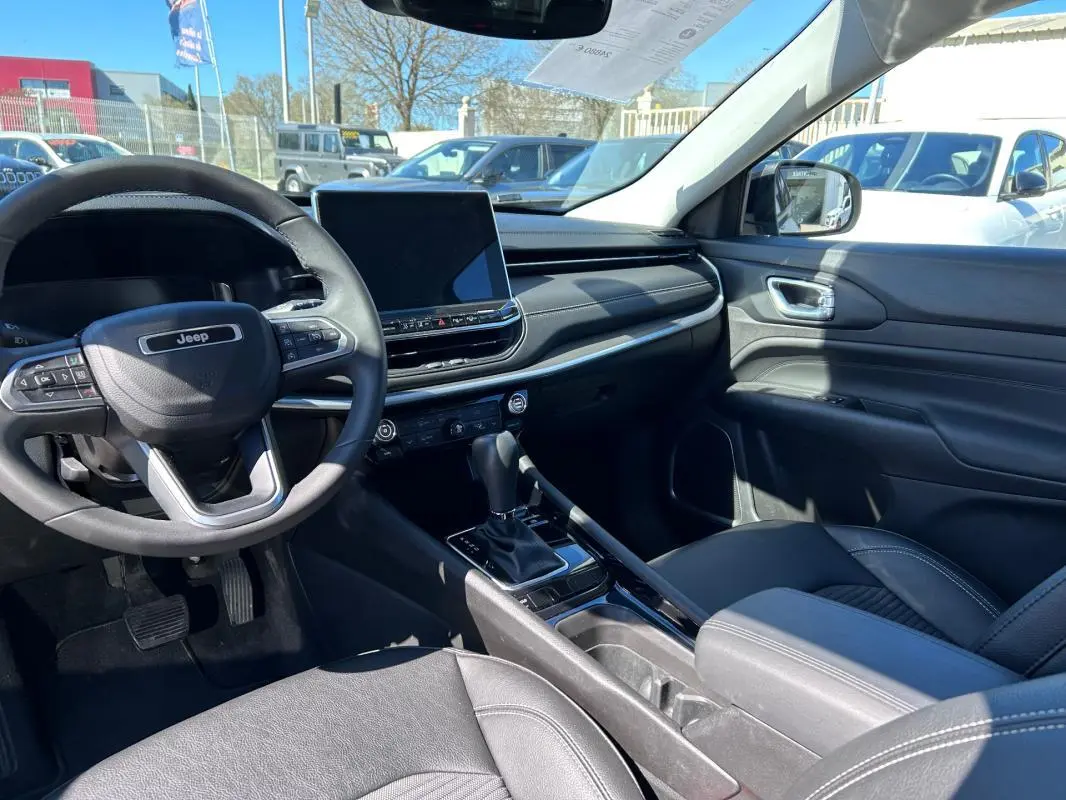 Vue intérieure côté conducteur du Jeep Compass 2024 gris, montrant volant, écran tactile et accoudoir central.
