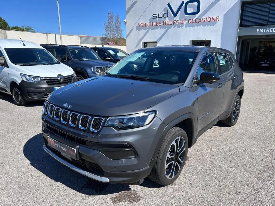 Jeep Compass gris en 3/4 avant droit, avec jantes alliage 18 pouces et calandre chromée, stationné devant un concessionnaire.