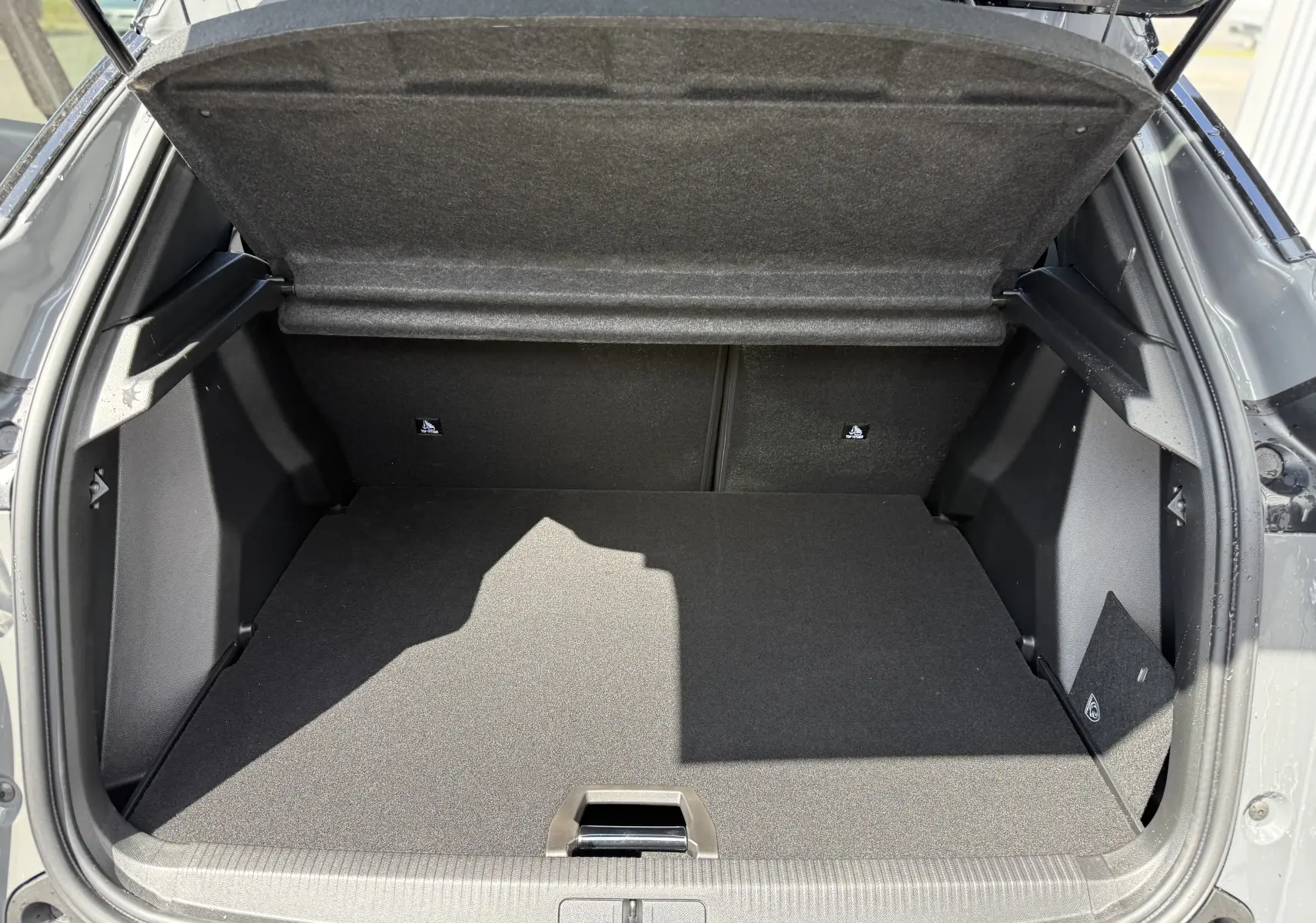 Coffre ouvert vu de l'arrière d'un Peugeot 2008 Hybrid gris selenium avec toit noir, montrant un espace de chargement vide.