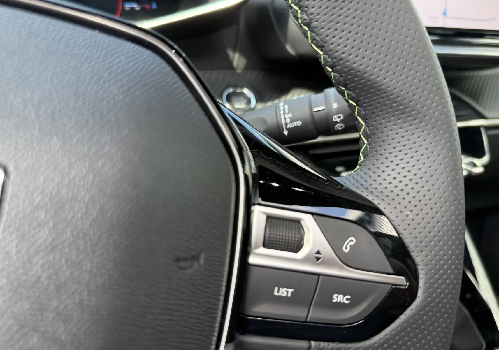 Détail du volant perforé avec surpiqûres vertes du Peugeot 2008 Hybrid 145ch GT, boutons de commande intégrés.