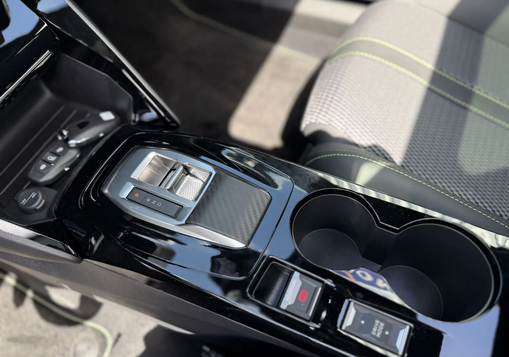 Vue rapprochée de la console centrale noire brillante du Peugeot 2008 Hybrid 145ch, avec levier de vitesse et porte-gobelets.