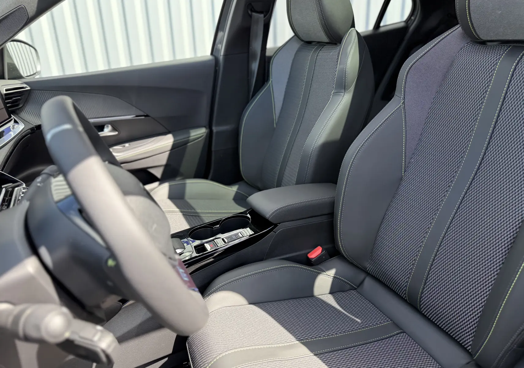 Vue intérieure côté conducteur du Peugeot 2008 Hybrid 145ch GT 2026, sièges en tissu et cuir noir avec surpiqûres vertes.