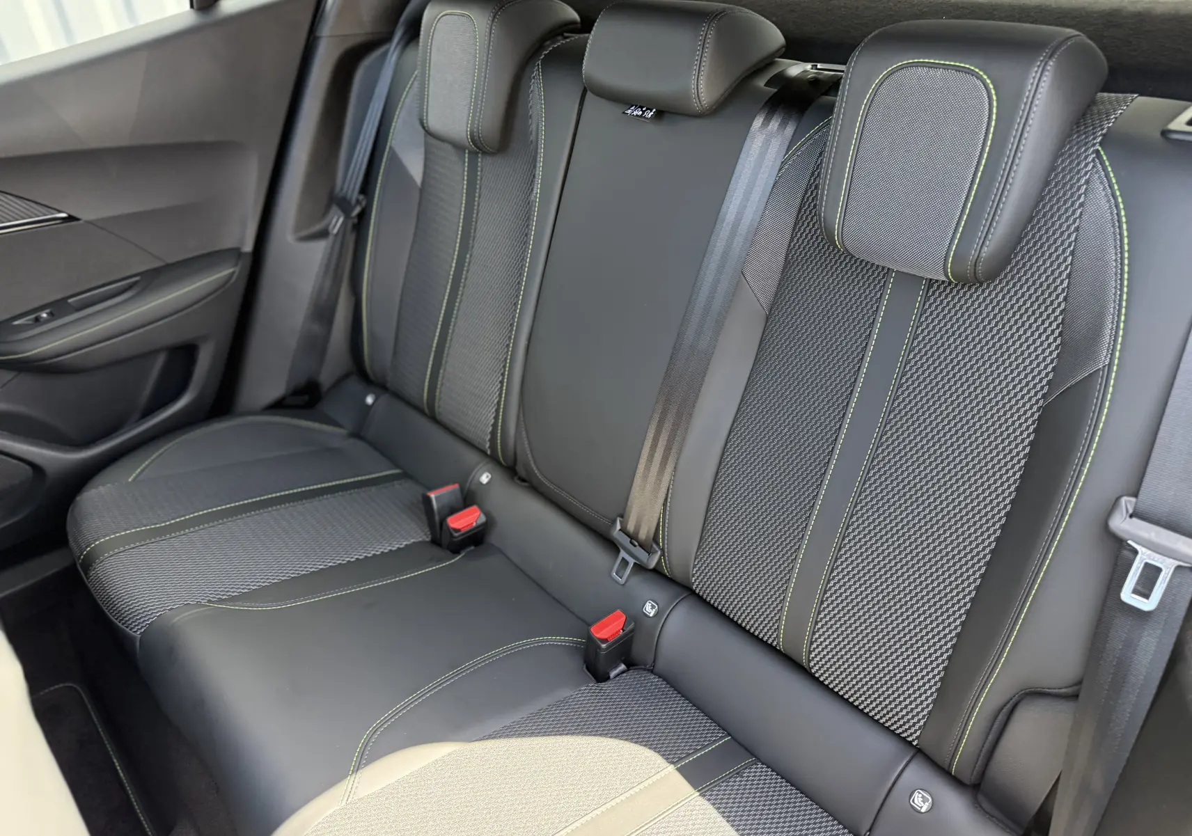 Vue intérieure du siège arrière droit du Peugeot 2008 Hybrid 145ch GT, tissu noir avec surpiqûres vertes contrastantes.