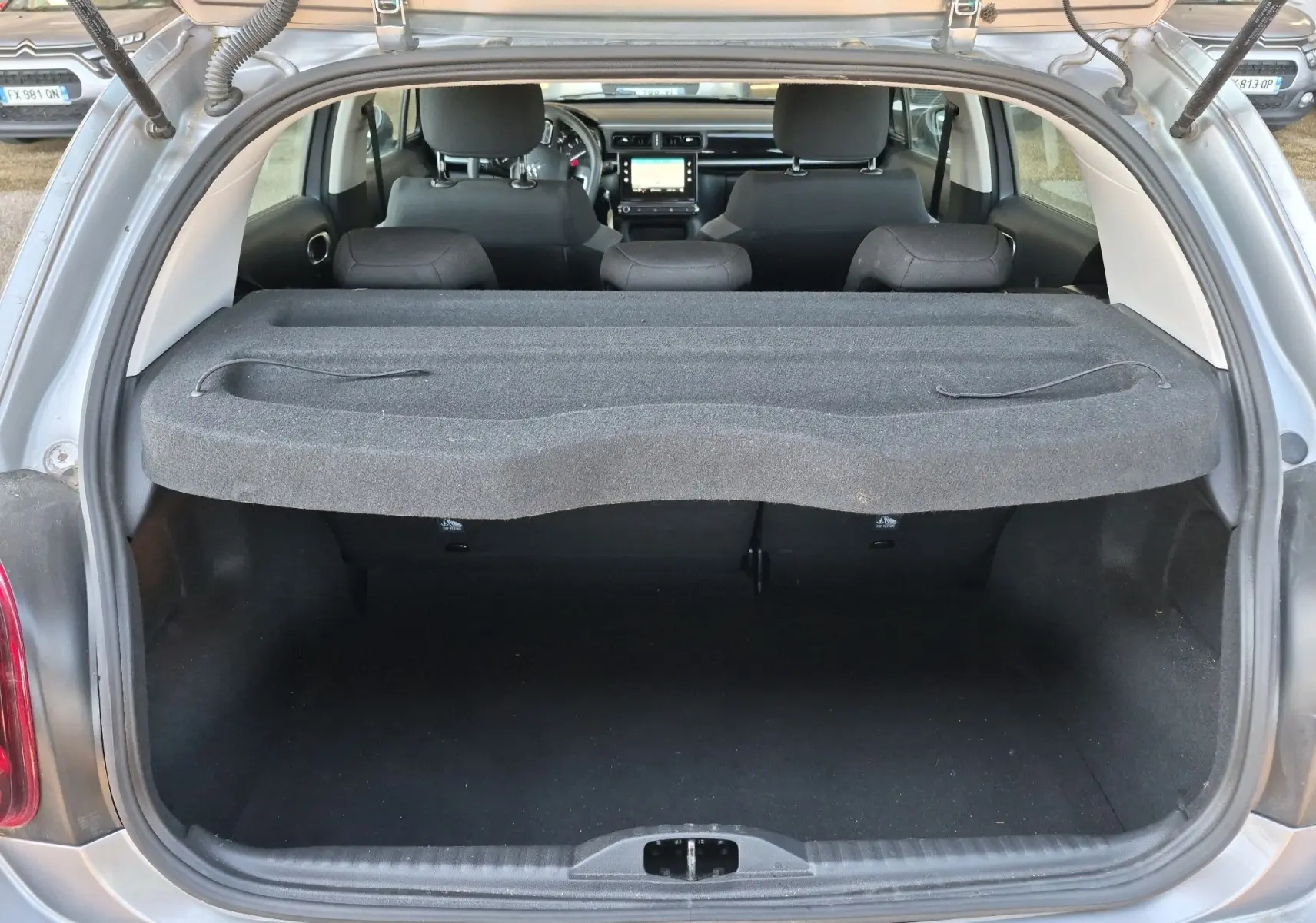 Coffre ouvert vu de l'arrière d'une Citroën C3 gris Artense, avec tablette cache-bagages et intérieur noir visible.