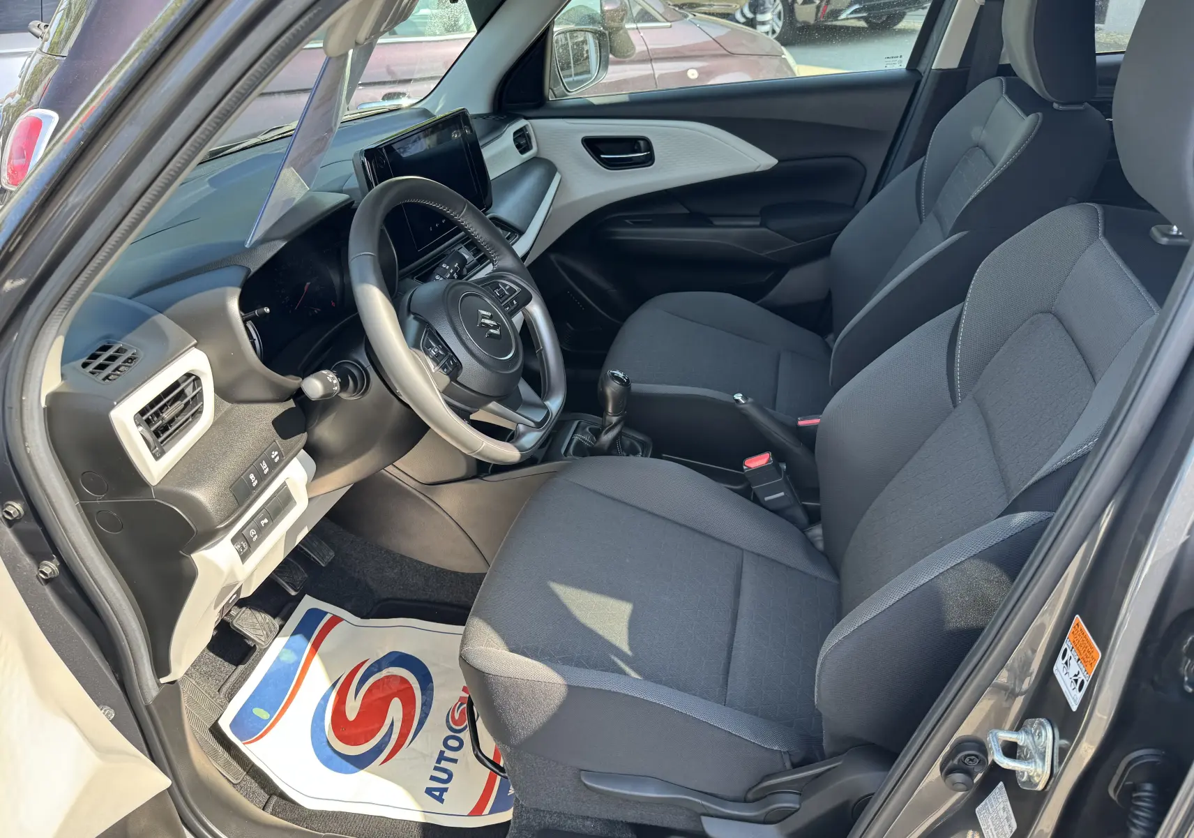Vue intérieure côté conducteur de la Suzuki Swift 1.2 Privilège Hybrid 2025, sièges tissu gris et tableau de bord moderne.